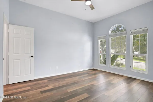 an empty room with wooden floor fan and windows