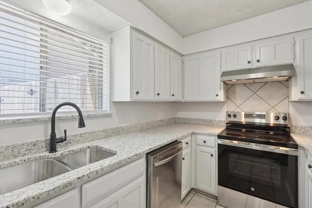a kitchen with stainless steel appliances granite countertop white cabinets a stove a sink and dishwasher