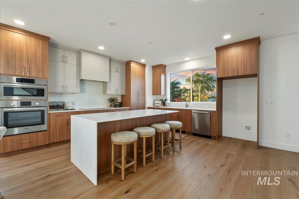 3243 West Moore Street Boise, ID 83702 - Photo 6 of 38 Kitchen with brown cabinetry, a breakfast bar area, a center island, light wood-type flooring, and appliances with stainless steel finishes