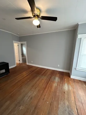 an empty room with wooden floor fan and windows