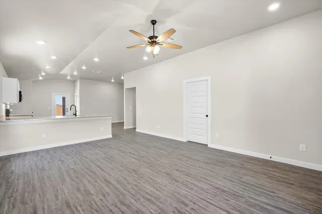 a view of an empty room with wooden floor and a ceiling fan
