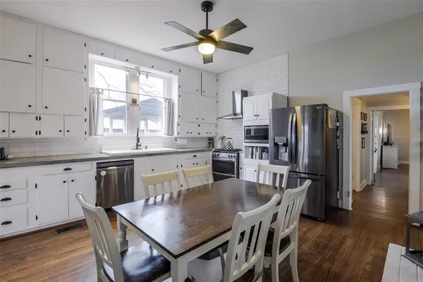 a kitchen with stainless steel appliances granite countertop a stove a refrigerator a sink a dining table and chairs with wooden floor