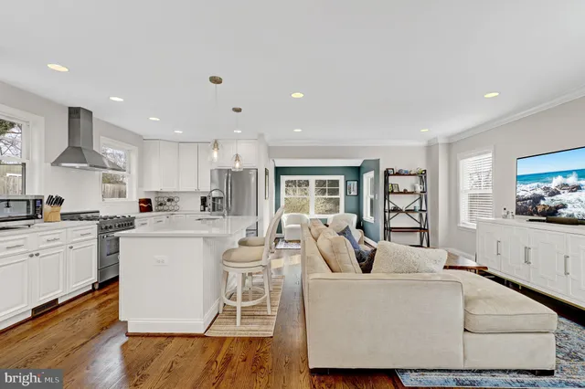 a living room with white couches and kitchen view with wooden floor