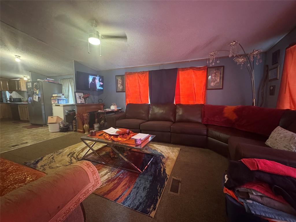 1614 Cole Road Bellmead, TX 76705 - Photo 2 of 21 Spacious living area featuring a ceiling fan with integrated lighting, wood-finish flooring, and a partial view of the kitchen with stainless steel appliances