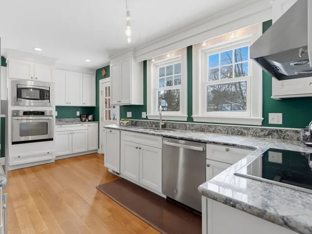 a kitchen with stainless steel appliances granite countertop a sink and a stove top oven with wooden floor