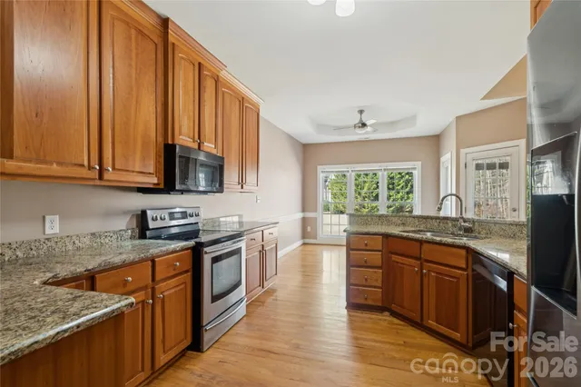 a kitchen with stainless steel appliances granite countertop wooden cabinets a sink dishwasher a stove and a refrigerator with wooden floor