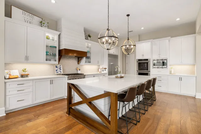 a kitchen with stainless steel appliances kitchen island granite countertop a stove a sink a refrigerator and white cabinets with wooden floor