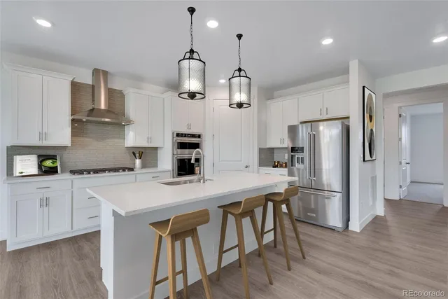 a kitchen with stainless steel appliances granite countertop a sink a stove a refrigerator and white cabinets with wooden floor