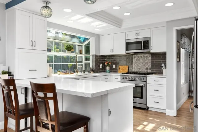 a kitchen with stainless steel appliances granite countertop a stove top oven a refrigerator a sink and white cabinets with wooden floor