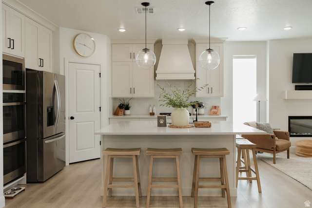 629 Spring Lily Drive St. George, UT 84790 - Photo 6 of 50 Open-concept kitchen featuring an island with seating, stainless steel appliances, light-toned cabinetry, a built-in range hood, and wood-finish flooring