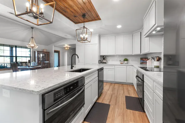 a kitchen with stainless steel appliances granite countertop a refrigerator a sink dishwasher a stove and a dining table with wooden floor