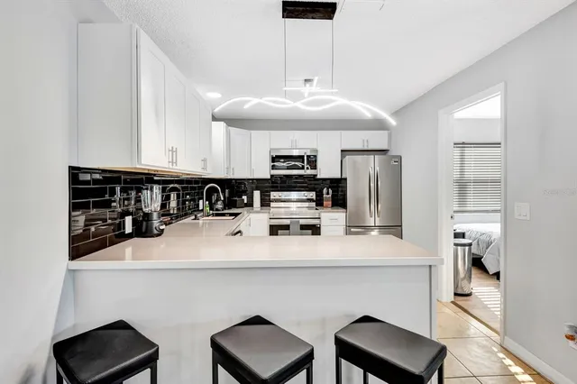 a kitchen with stainless steel appliances a dining table chairs refrigerator and sink