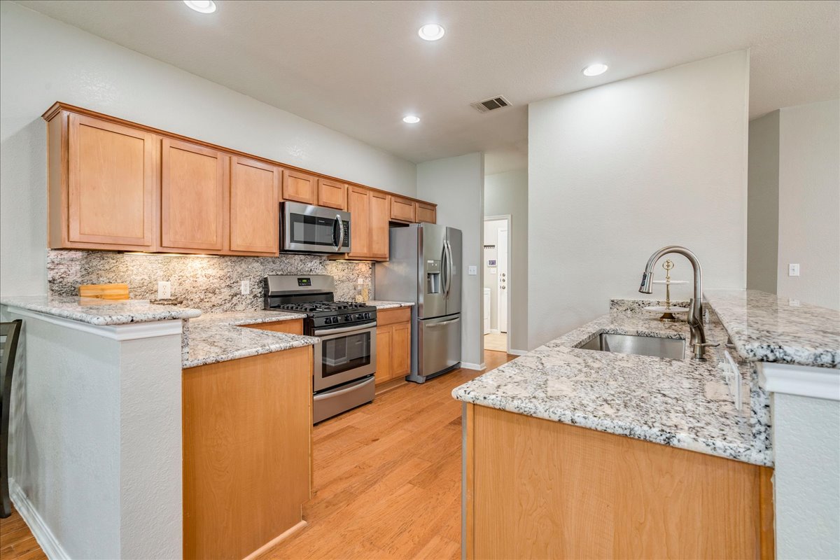 1151 Stone Rim Loop Buda, TX 78610 - Photo 12 of 36 This kitchen features granite countertops, wood cabinetry, stainless steel appliances, and hardwood flooring