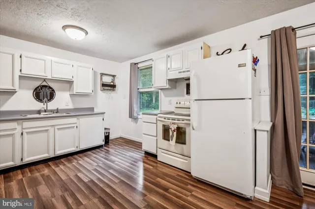 a kitchen with a refrigerator a stove top oven with white cabinets and wooden floor