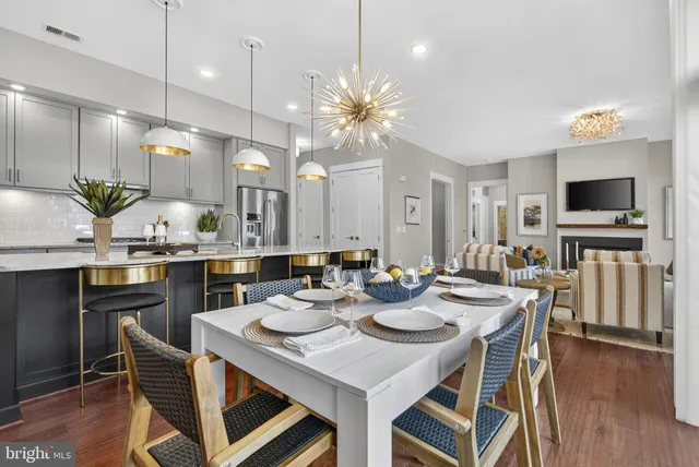 a kitchen with stainless steel appliances granite countertop a refrigerator a stove top oven a dining table and chairs with wooden floor