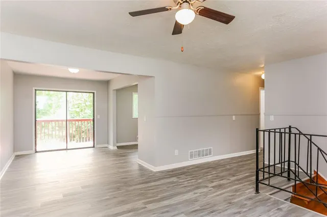 an empty room with wooden floor fan and windows