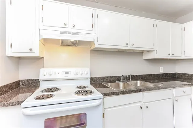 a kitchen with granite countertop a sink stove and white cabinets