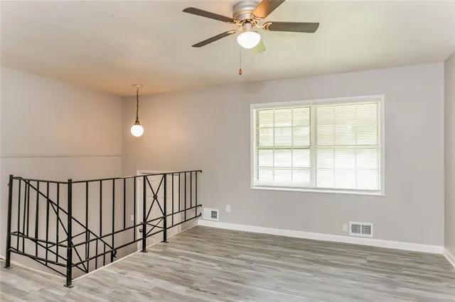 an empty room with wooden floor fan and windows