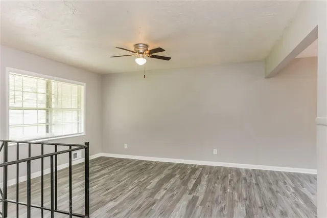 an empty room with wooden floor fan and windows