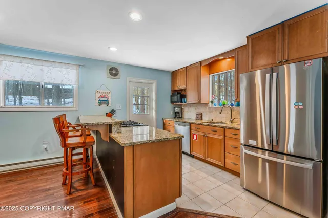 a kitchen with stainless steel appliances granite countertop a refrigerator a stove a sink dishwasher and a dining table with wooden floor