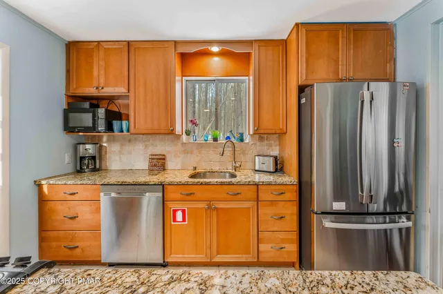 a kitchen with stainless steel appliances granite countertop a refrigerator a stove and a sink with wooden cabinets