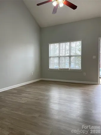 an empty room with wooden floor chandelier fan and windows