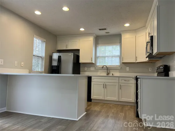 a kitchen with stainless steel appliances granite countertop a refrigerator a sink dishwasher a stove and white countertops with wooden floor