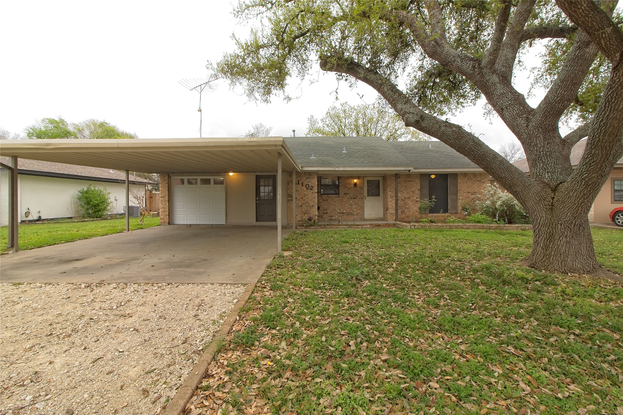 View of front of house featuring driveway, an attached carport, a front yard, a garage, and brick siding