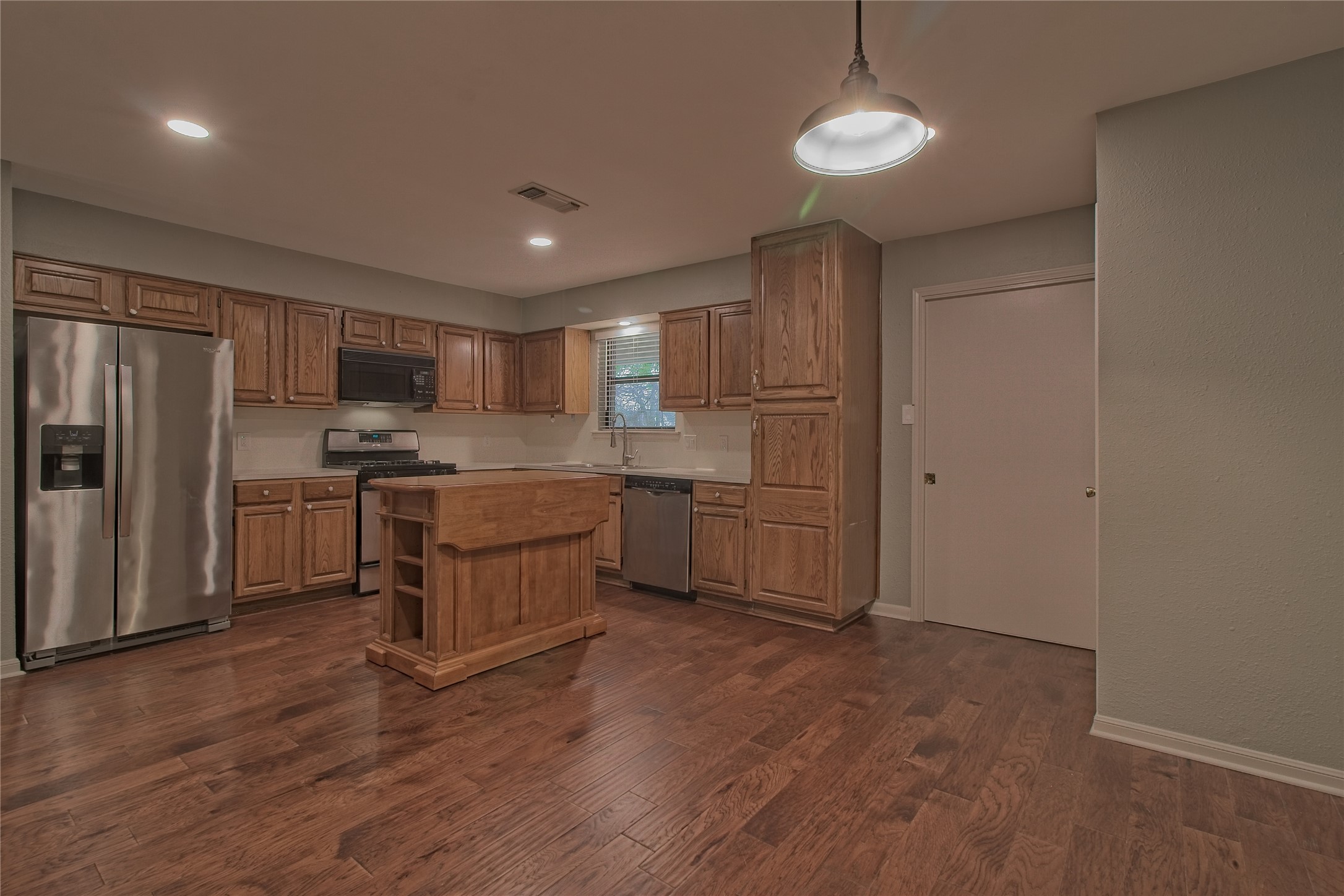 1102 Fowzer Street Taylor, TX 76574 - Photo 12 of 27 Kitchen featuring stainless steel appliances, light countertops, dark wood-style floors, a kitchen island, and wood finish cabinetry