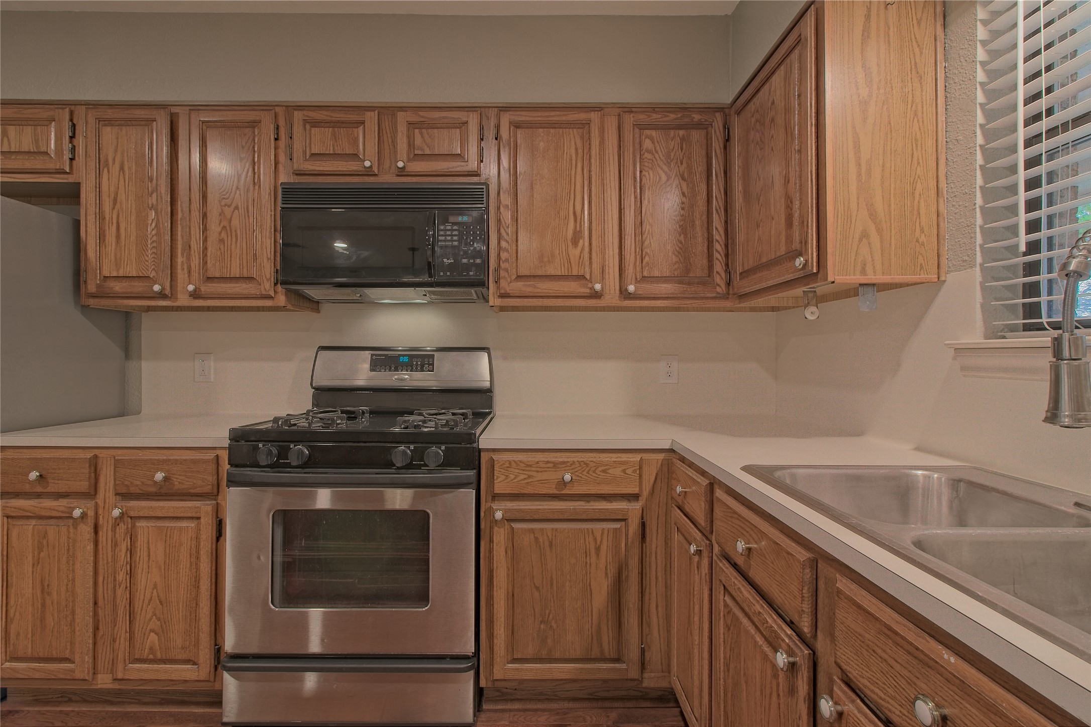 1102 Fowzer Street Taylor, TX 76574 - Photo 14 of 27 Kitchen featuring stainless steel range with gas stovetop, black microwave, light countertops, wood finish cabinetry, and freestanding refrigerator