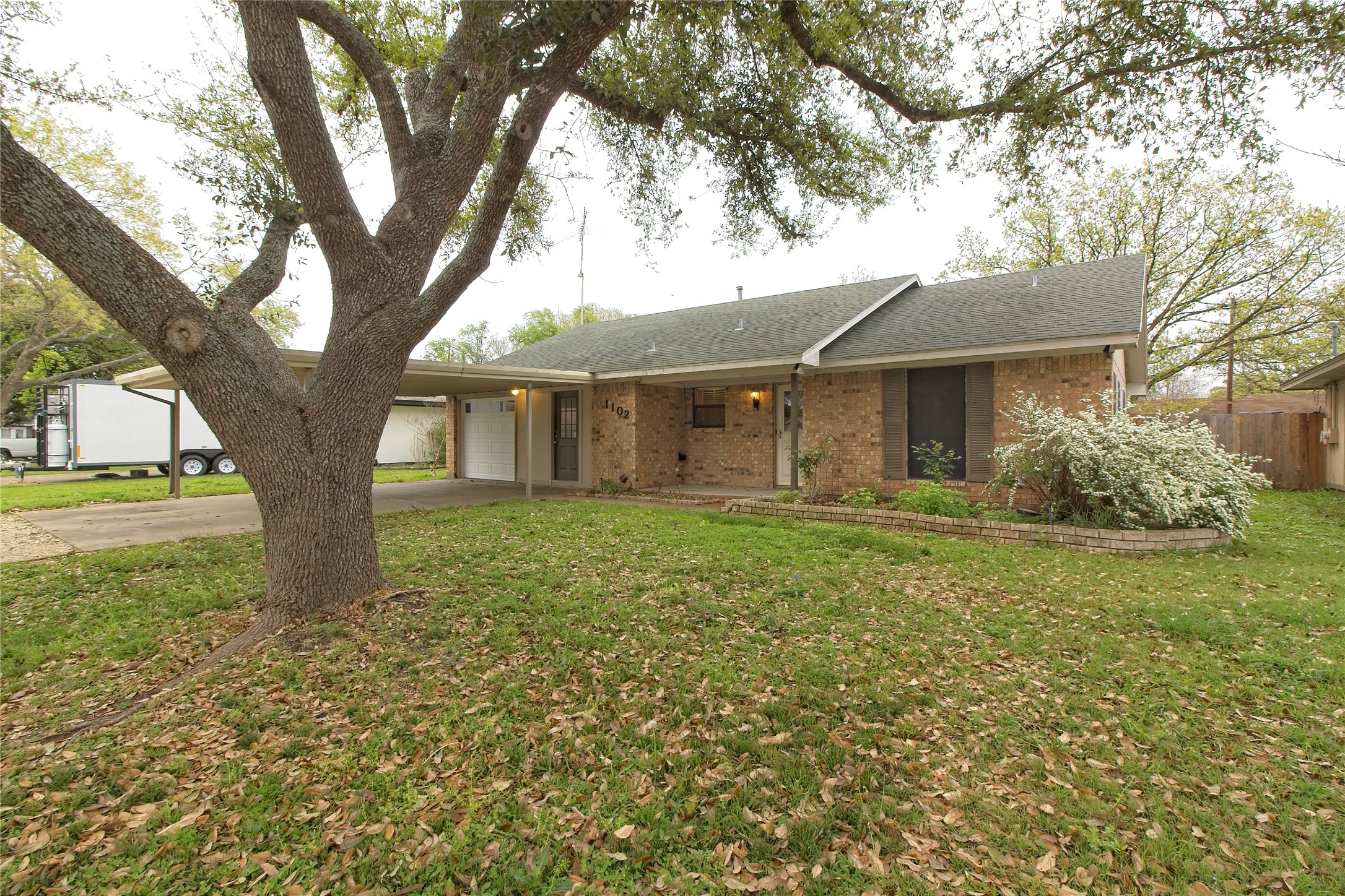 1102 Fowzer Street Taylor, TX 76574 - Photo 2 of 27 Ranch-style home featuring brick siding, a front lawn, a garage, concrete driveway, and a shingled roof