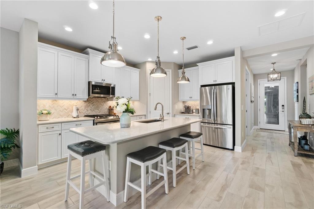 2298 Marquesa Circle Naples, FL 34112 - Photo 3 of 50 a kitchen with stainless steel appliances kitchen island a island a stove a refrigerator and white cabinets with wooden floors