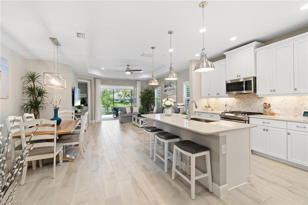 2298 Marquesa Circle Naples, FL 34112 - Photo 5 of 50 a kitchen with cabinets a sink dishwasher a stove and a dining table with wooden floor