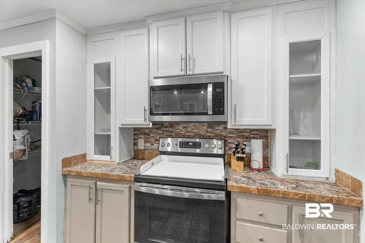 21011 River Road Robertsdale, AL 36567 - Photo 9 of 29 Kitchen featuring white upper cabinetry, a stainless steel microwave and range, a tiled backsplash, and stone-finish countertops