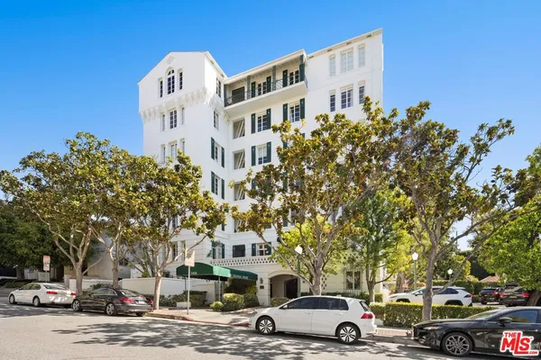 a front view of a building with lot of cars and trees