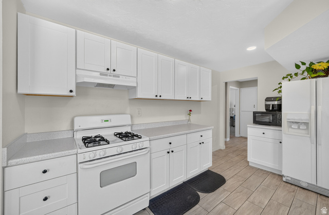 4468 North Droubay Road Tooele, UT 84074 - Photo 11 of 60 White cabinetry with black hardware, light-toned countertops, white range oven, and wood-finish tile flooring