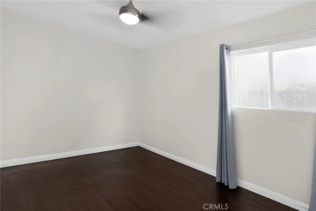 a view of an empty room with wooden floor and a ceiling fan