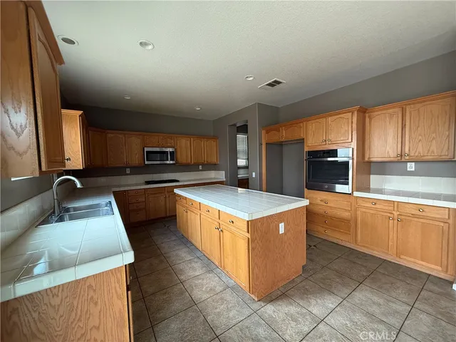 a kitchen with stainless steel appliances granite countertop wooden cabinets a sink a stove a refrigerator and island