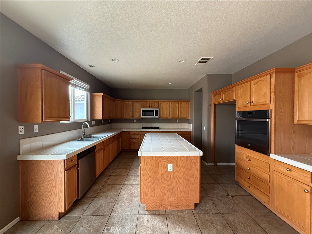 1264 Reisling Drive Perris, CA 92571 - Photo 4 of 15 a large kitchen with stainless steel appliances kitchen island granite countertop a large counter top and wooden cabinets