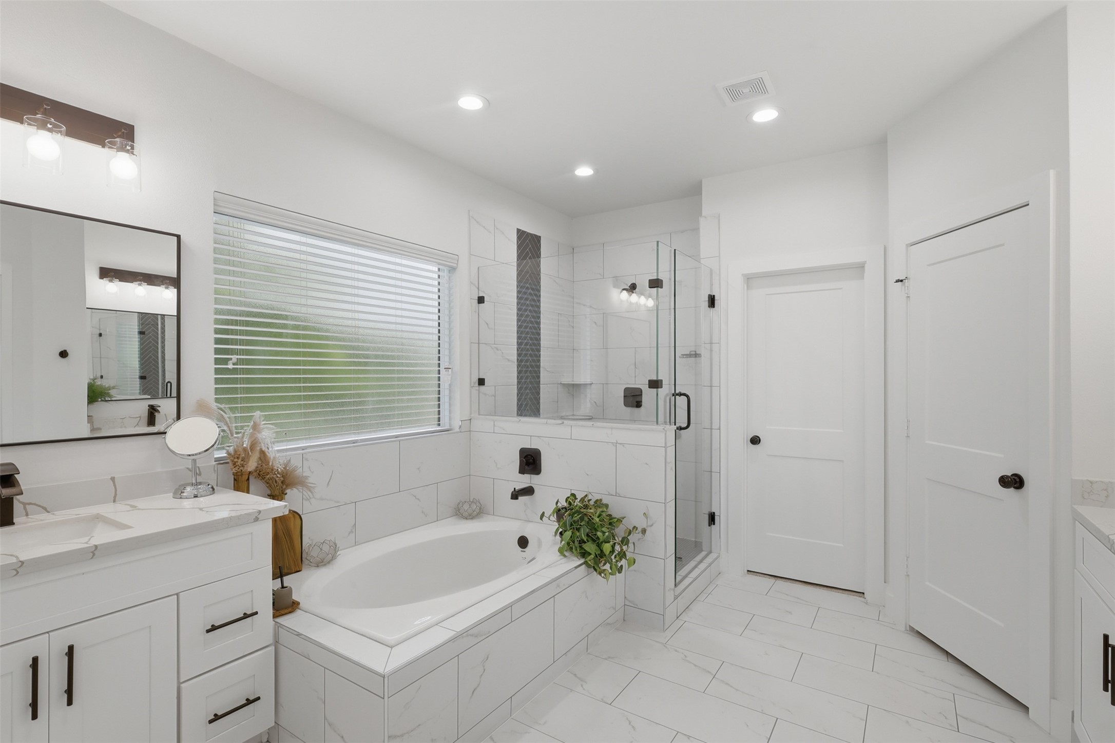 6833 Paris Street Houston, TX 77021 - Photo 21 of 23 This modern bathroom features a sleek, white design with a spacious bathtub, a glass-enclosed shower, and ample cabinetry. Natural light streams through a large window, creating a bright and inviting space.