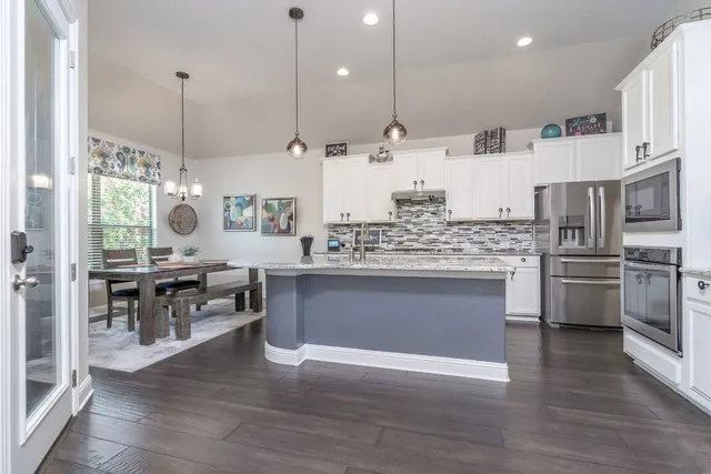 a kitchen with stainless steel appliances kitchen island granite countertop a stove a sink a refrigerator and a oven with wooden floor