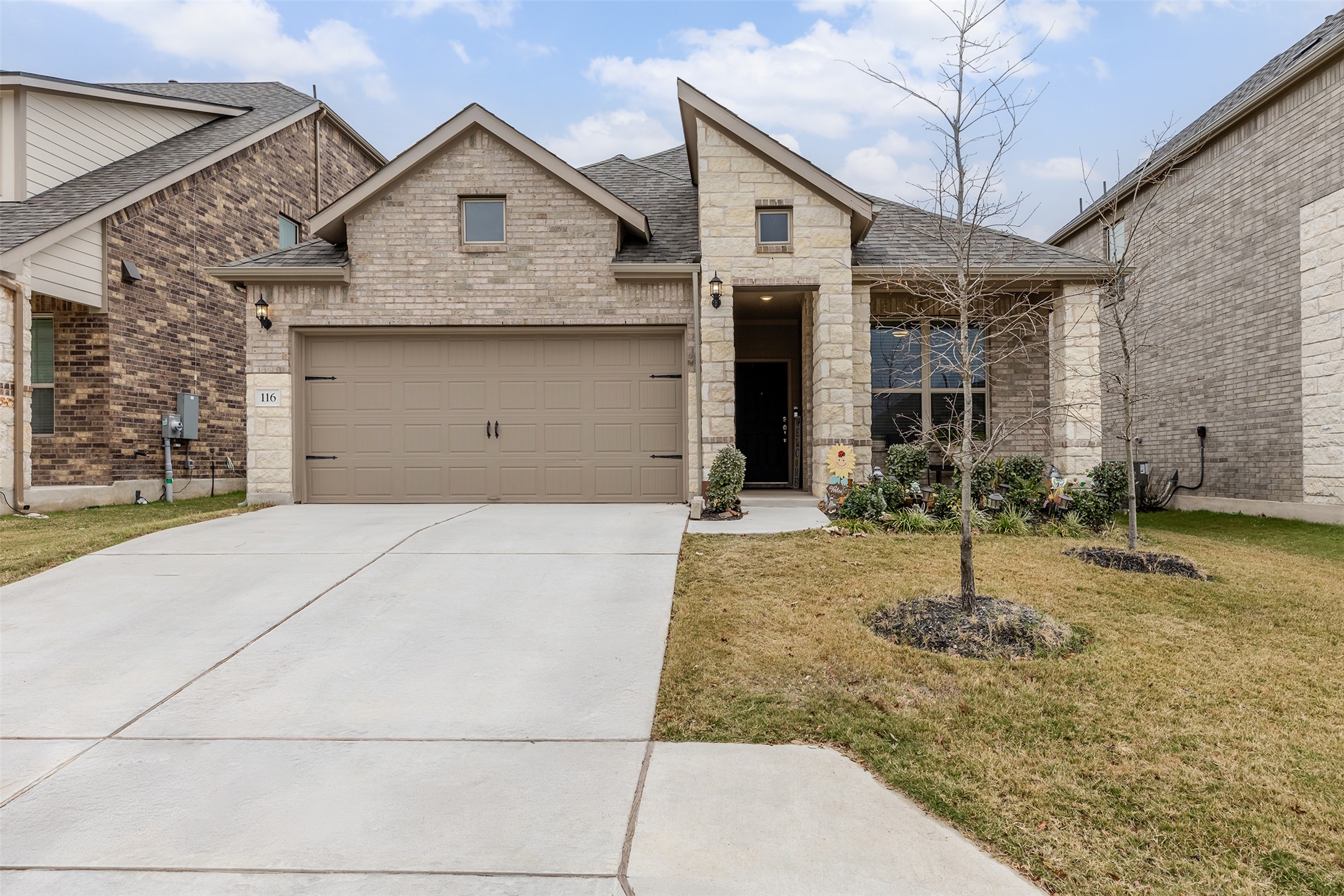 View of front of home featuring roof with shingles, stone siding, concrete driveway, and a front yard