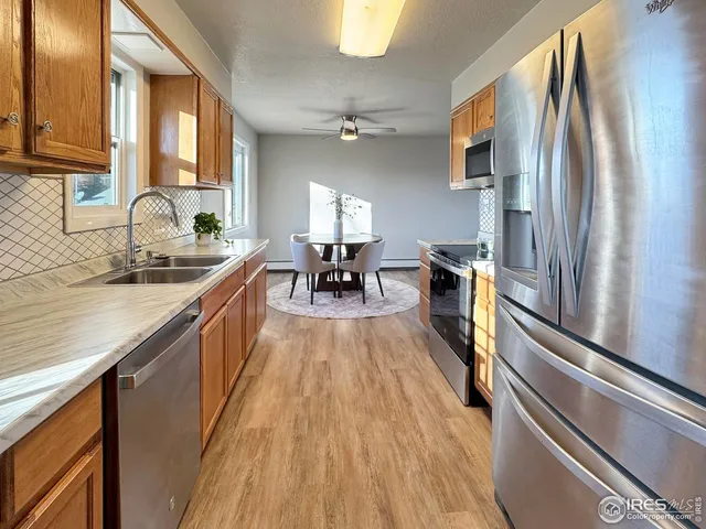 a kitchen with stainless steel appliances granite countertop a refrigerator a sink dishwasher a stove and white countertops with wooden floor