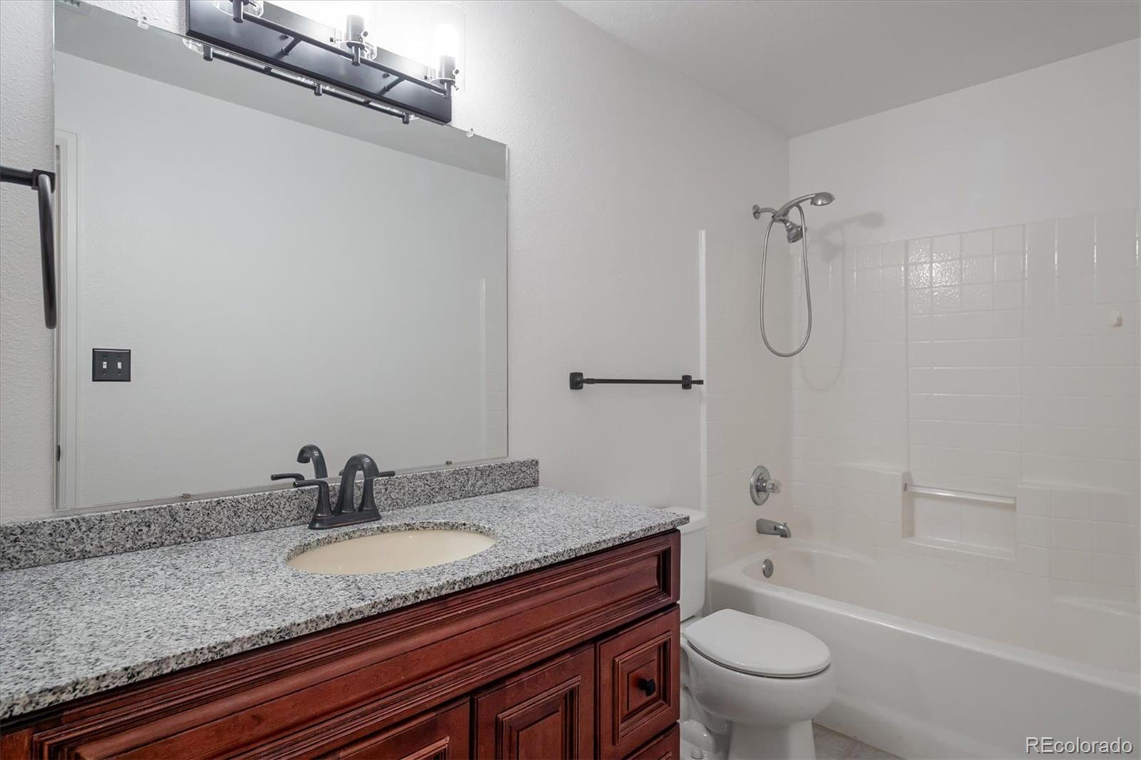 3855 East Canyon Ranch Road, Unit 104 Highlands Ranch, CO 80126 - Photo 16 of 18 a bathroom with a granite countertop sink a toilet and shower