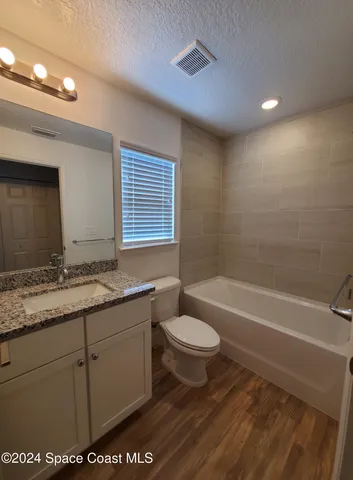 a bathroom with a granite countertop sink a toilet a mirror a bathtub and shower