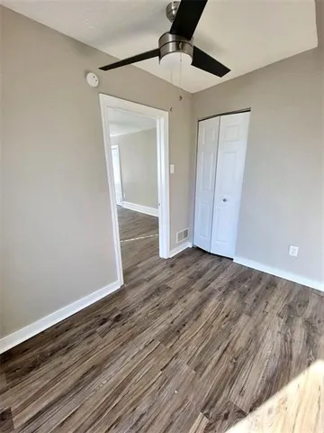 a view of an empty room with wooden floor and a ceiling fan
