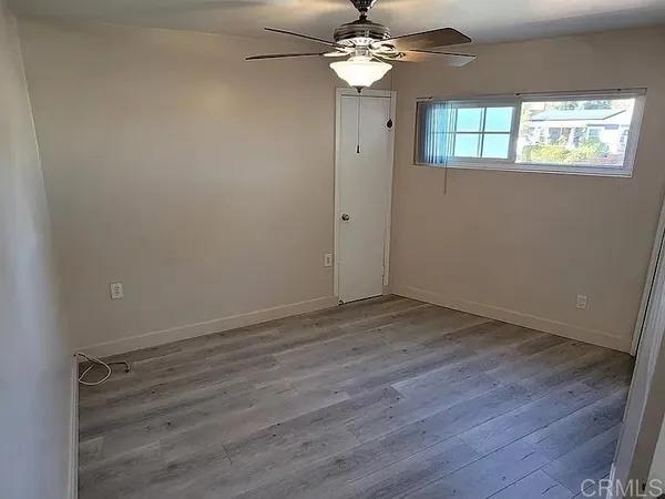 an empty room with wooden floor chandelier fan and windows