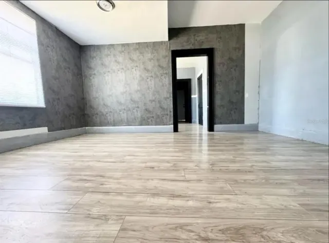 a view of an empty room with wooden floor and a window