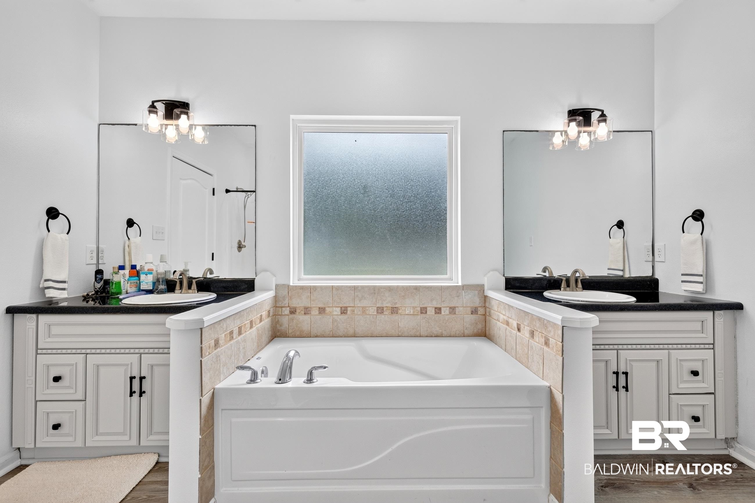 17419 Lewis Smith Drive Foley, AL 36535 - Photo 24 of 38 Spacious bathroom featuring a built-in tub with tile surround, two separate vanities with undermount sinks, dark countertops, and individual mirrors with contemporary light fixtures