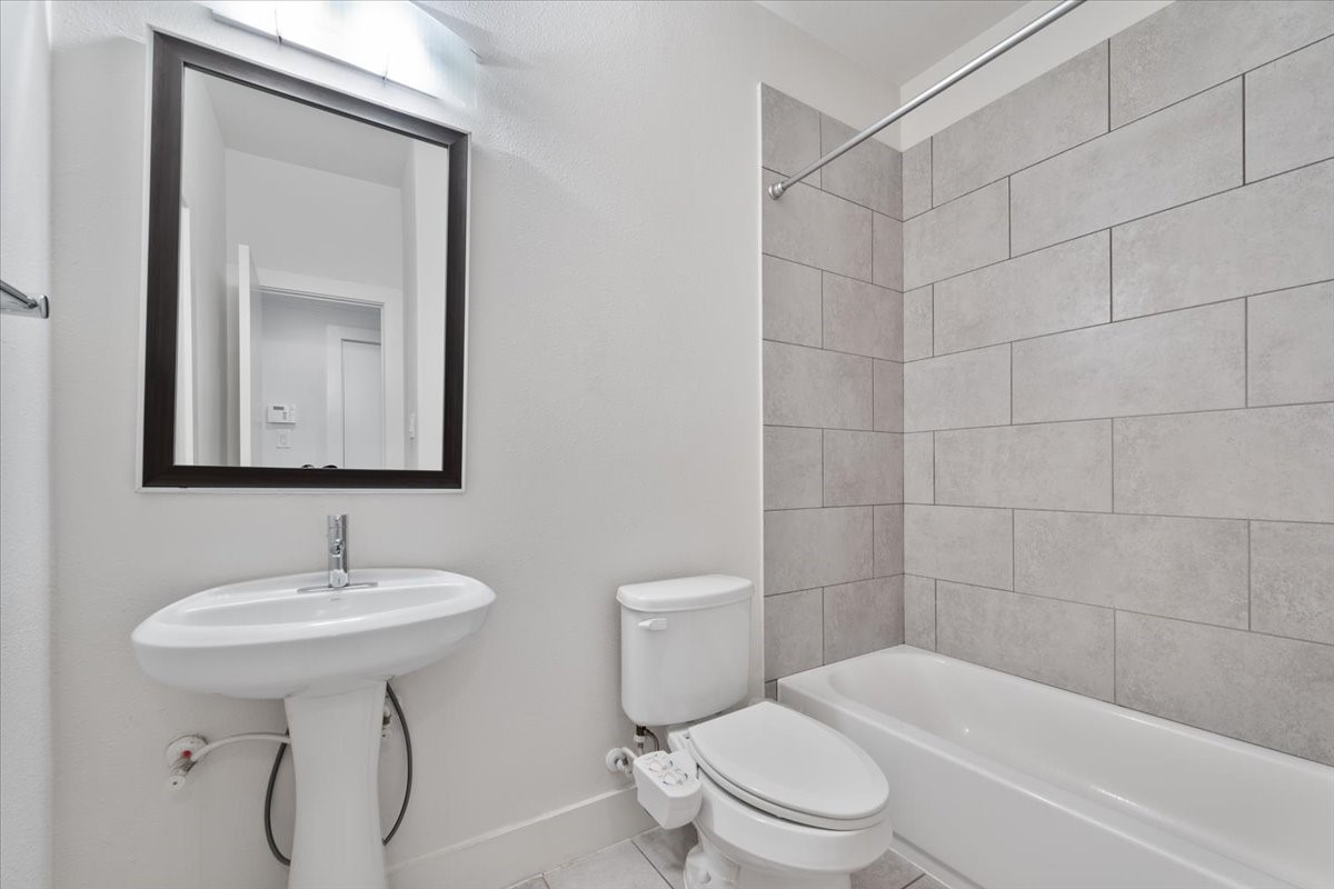 1333 West 22nd Street, Unit F Houston, TX 77008 - Photo 14 of 22 This bathroom features a modern, clean design with a pedestal sink, toilet, and a bathtub with a tiled shower surround. The neutral color palette enhances the bright, spacious feel.